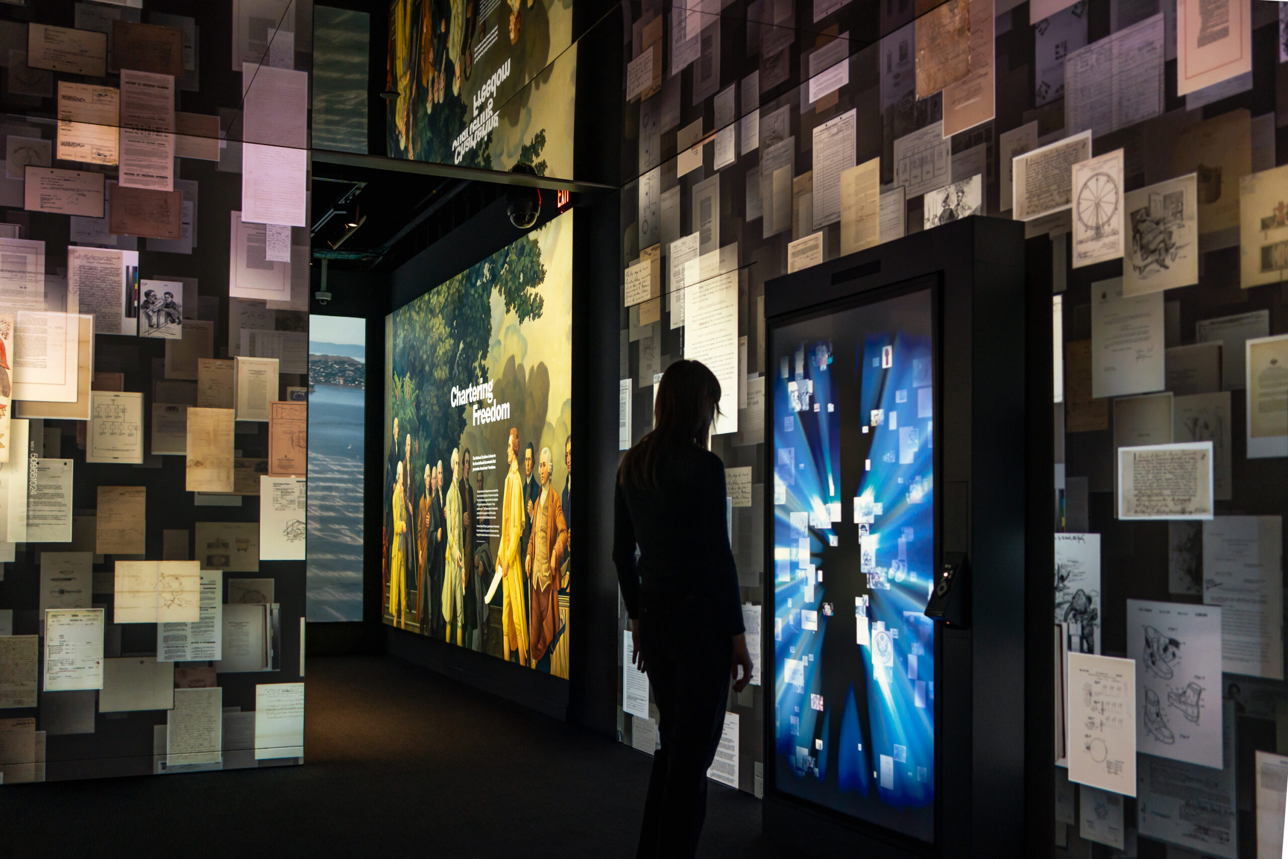 a shadow in front of many large scale screens that depict literal pages, which represent the United States's founding documents